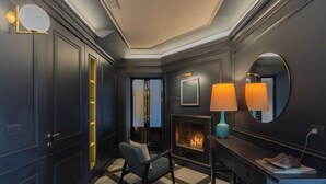Ein modernes Hotelzimmer mit dunklen Wänden, einem Schachbrettmuster-Boden, einem Kamin und einer Sitzecke mit einem Sessel und einem Tisch.