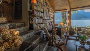 A cozy room with a wooden staircase, a bookshelf, a comfortable sofa, and a view of a lake and mountains.