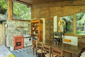 A rustic kitchen with a stone fireplace, wooden shelves, and a large window overlooking greenery. - The Writer's Nest by Rent all Como (Faggeto Lario)