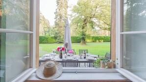 A dining area with a table set for four, a large window, and a view of a garden. - Villa Riva Bellagio With Pool by Rent all Como (Bellagio)