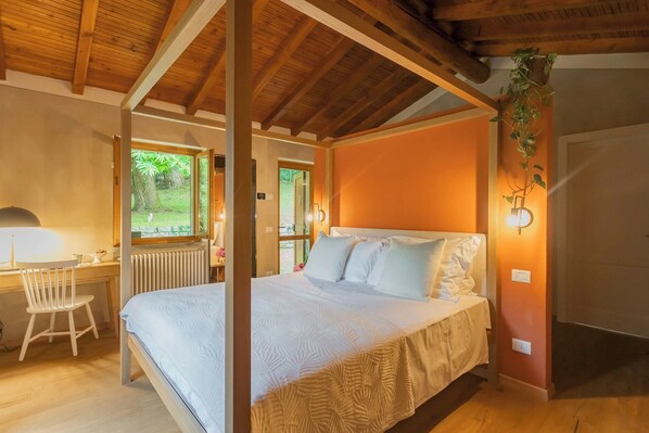 A bedroom with a wooden ceiling, a bed with white bedding, a desk with a chair, and a window with a view of greenery. - Villa Riva Bellagio With Pool by Rent all Como (Bellagio)