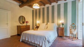 Un dormitorio con cama, cabecera de madera, dos mesitas de noche con lámparas, un espejo y pared a rayas.