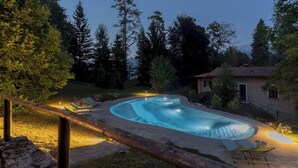 A swimming pool with a curved edge, surrounded by a wooden deck and lounge chairs. - Villa Riva Bellagio With Pool by Rent all Como (Bellagio)