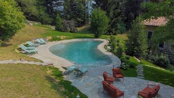 Una piscina de borde curvo, rodeada por una terraza de piedra y sillones reclinables verdes.