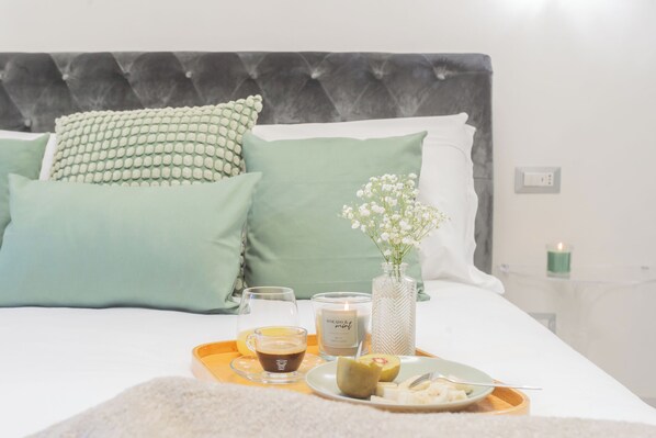 A neatly made bed with green pillows, a bedside table with a candle, a tray with a glass of coffee, and a plate with food. - Cernobbio Dream Suites by Rent all Como (Cernobbio)