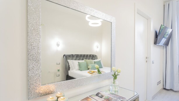 A bedroom with a large mirror, a bed with green pillows, a bedside table with candles, and a magazine. - Cernobbio Dream Suites by Rent all Como (Cernobbio)