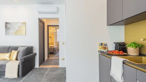 Ett modernt kök med grå skåp, en diskho och en bänkskiva med en kaffebryggare, en korg med tomater och en växt.