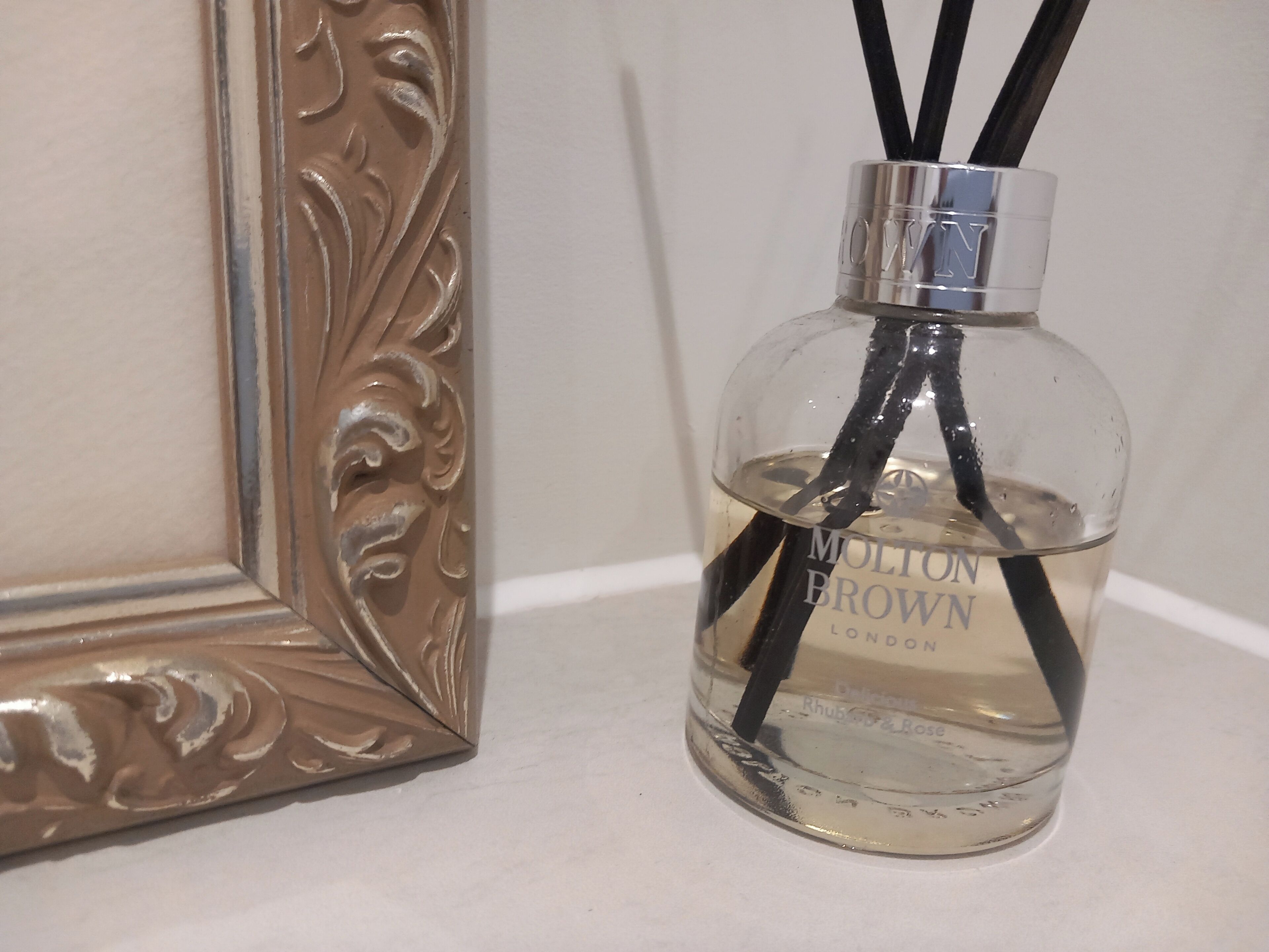A clear glass bottle with black straws and the label "MOLTON BROWN LONDON" on a white surface.