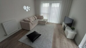 A modern living room with a sectional sofa, a flat-screen TV, and a small side table. - Tranquil Loughton Apartment Retreat (Loughton)