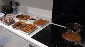 A kitchen with a modern induction cooktop, a variety of food dishes on the counter, and a pot on the stove. - Tranquil Loughton Apartment Retreat (Loughton)