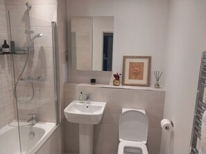 A modern bathroom with a glass-enclosed shower, a pedestal sink, a toilet, and a framed picture on the wall.