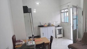 A compact kitchen with white cabinets, a gas stove, and a refrigerator. There is a dining table with chairs and a small window providing natural light.