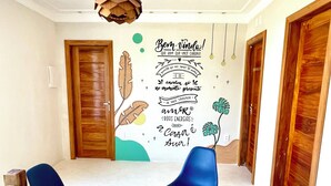 Une pièce avec une porte en bois, une chaise bleue, un luminaire suspendu et un mur orné d’un motif décoratif.