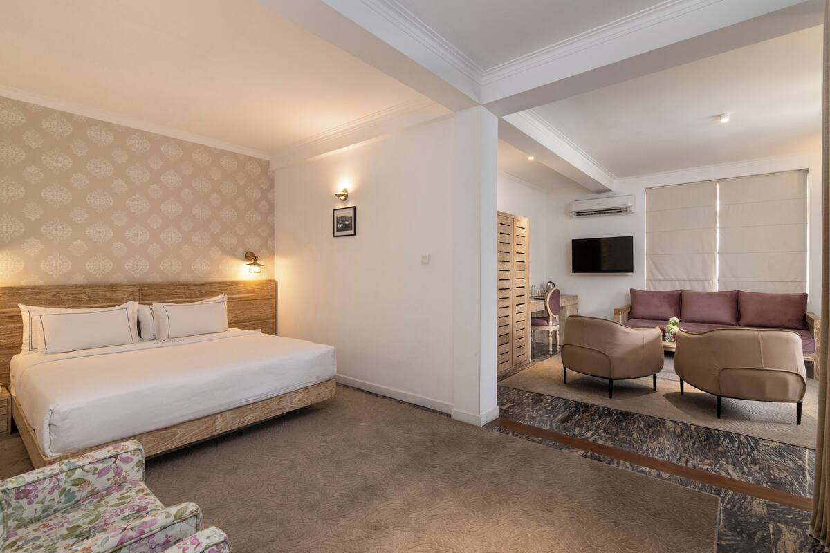 A hotel room with a large bed, a sofa, a chair, and a TV.