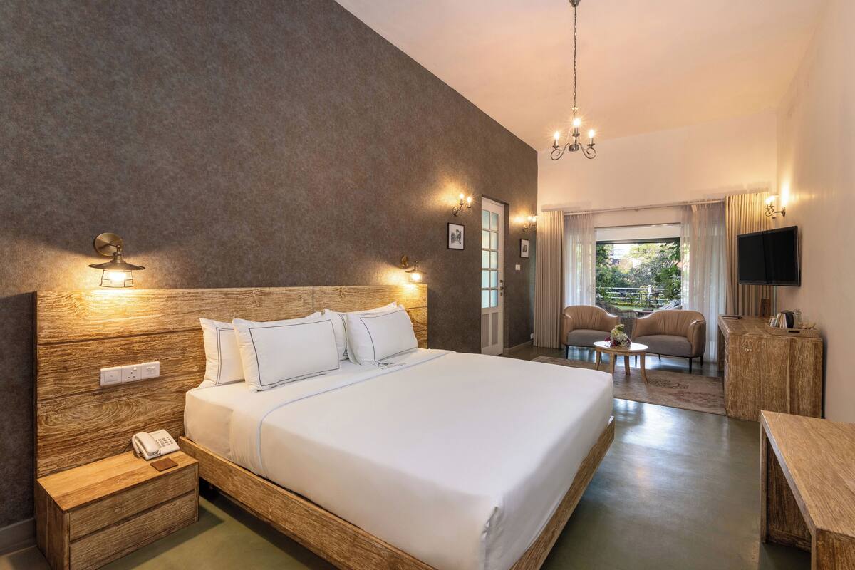 A hotel room with a large bed, bedside lamps, a wooden nightstand, a small table, and a TV on the wall.