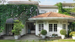 Un bâtiment blanc doté d’un toit incurvé, entouré d’un jardin agrémenté de plantes en pot et d’un chemin pavé.