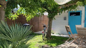 Una terraza de madera con una planta en maceta, una bicicleta y una puerta azul al fondo.
