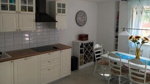 A kitchen with white cabinets, a wine rack, a clock, and a dining area with a table and chairs. - Holiday Home Jan (Stara Novalja)