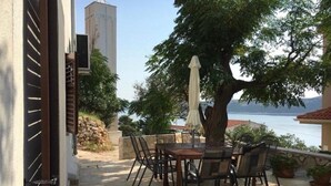 An outdoor patio with a table and chairs, a tree, and a view of the sea. - Holiday Home Jan (Stara Novalja)