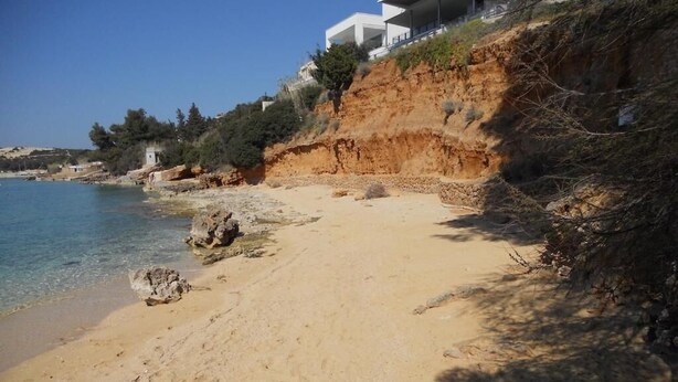 A sandy beach with a rocky cliff and a white building with balconies overlooking the sea. - Holiday Home Jan (Stara Novalja)