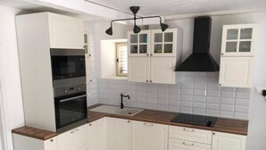 A kitchen with white cabinets, a black range hood, and a wooden countertop. - Holiday Home Jan (Stara Novalja)