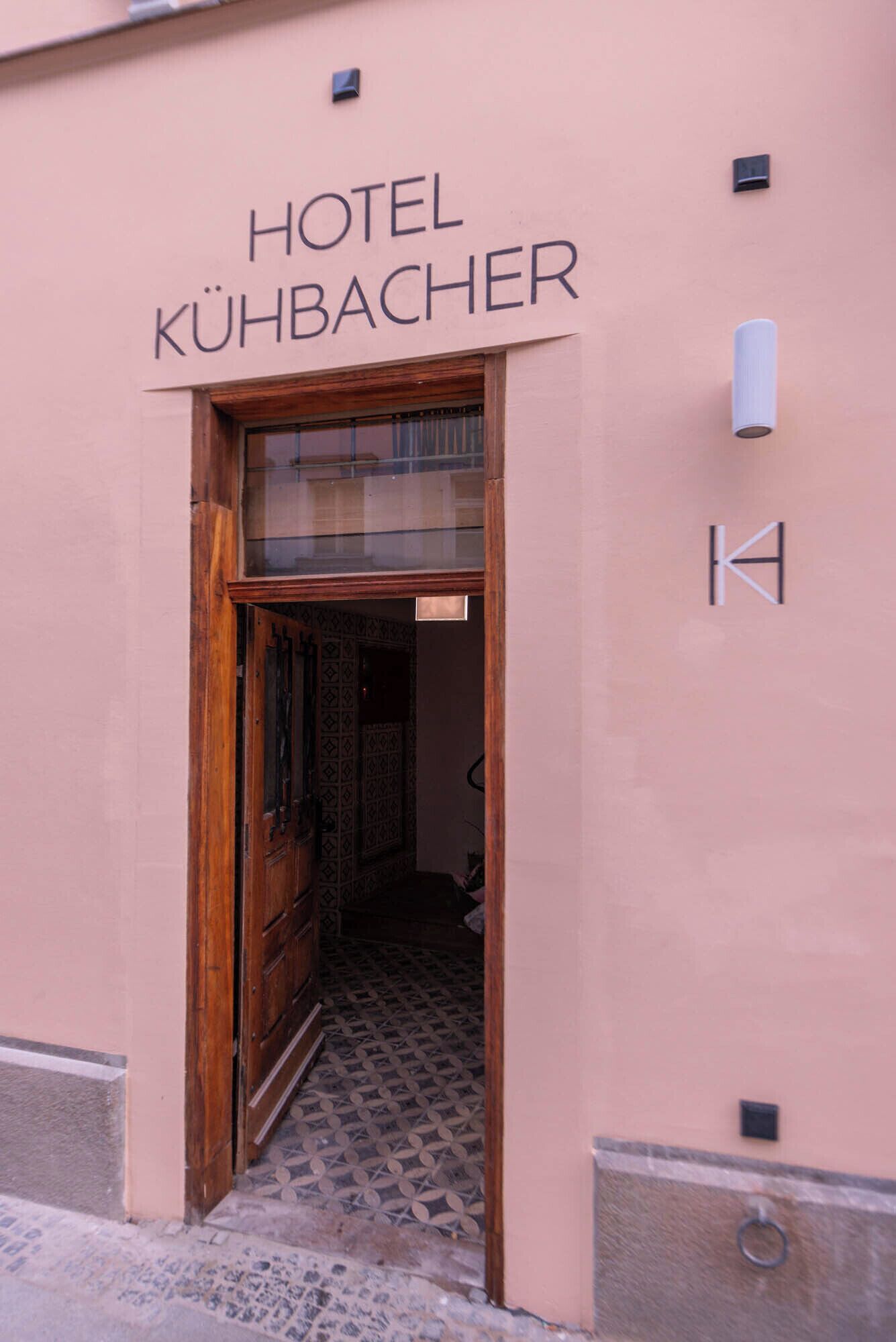 La entrada del Hotel Kühbacher, con una puerta de madera y baldosas de suelo con diseño.