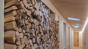 A hallway with a wooden wall of stacked logs, skylights, and a wooden floor. - Hotel Kühbacher (Passau)