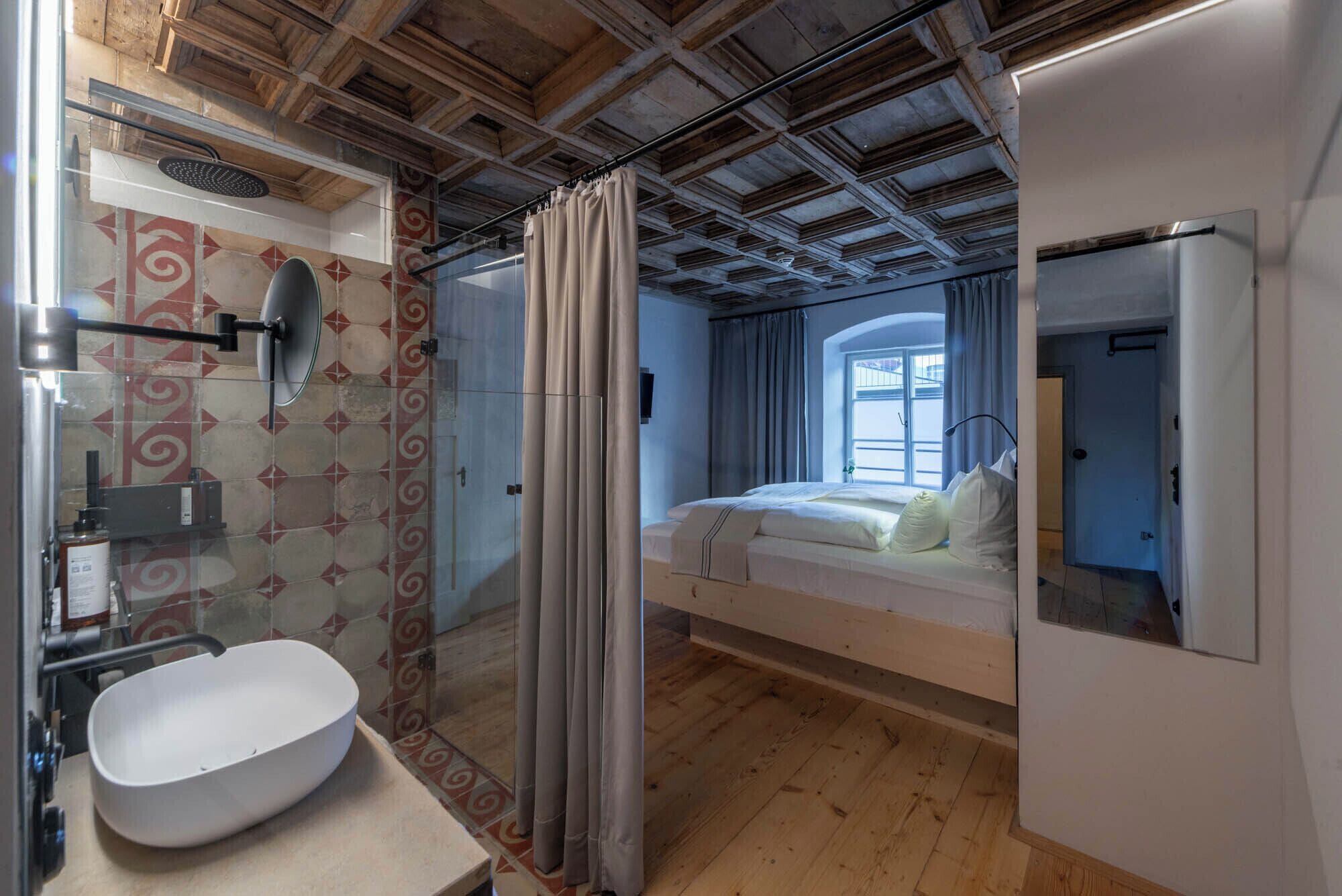 Un dormitorio con cama, ducha y baño con lavamanos y espejo.