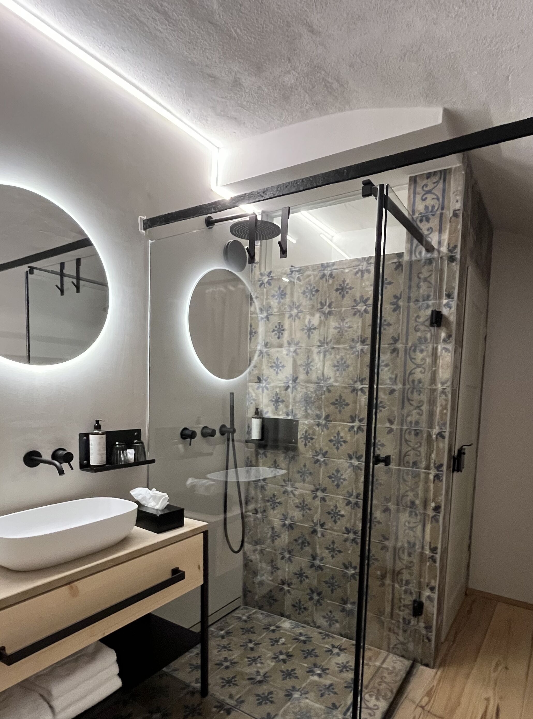 Une salle de bain moderne avec une douche à parois de verre, un miroir rond, un lavabo blanc et un porte-serviettes.