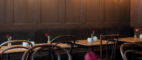 A restaurant interior with wooden tables and chairs, some with rose vases.
