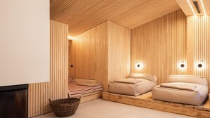 A modern spa room with wooden paneling, two massage beds, a small wicker basket, and a visible door leading to another area. - Hotel Kühbacher (Passau)
