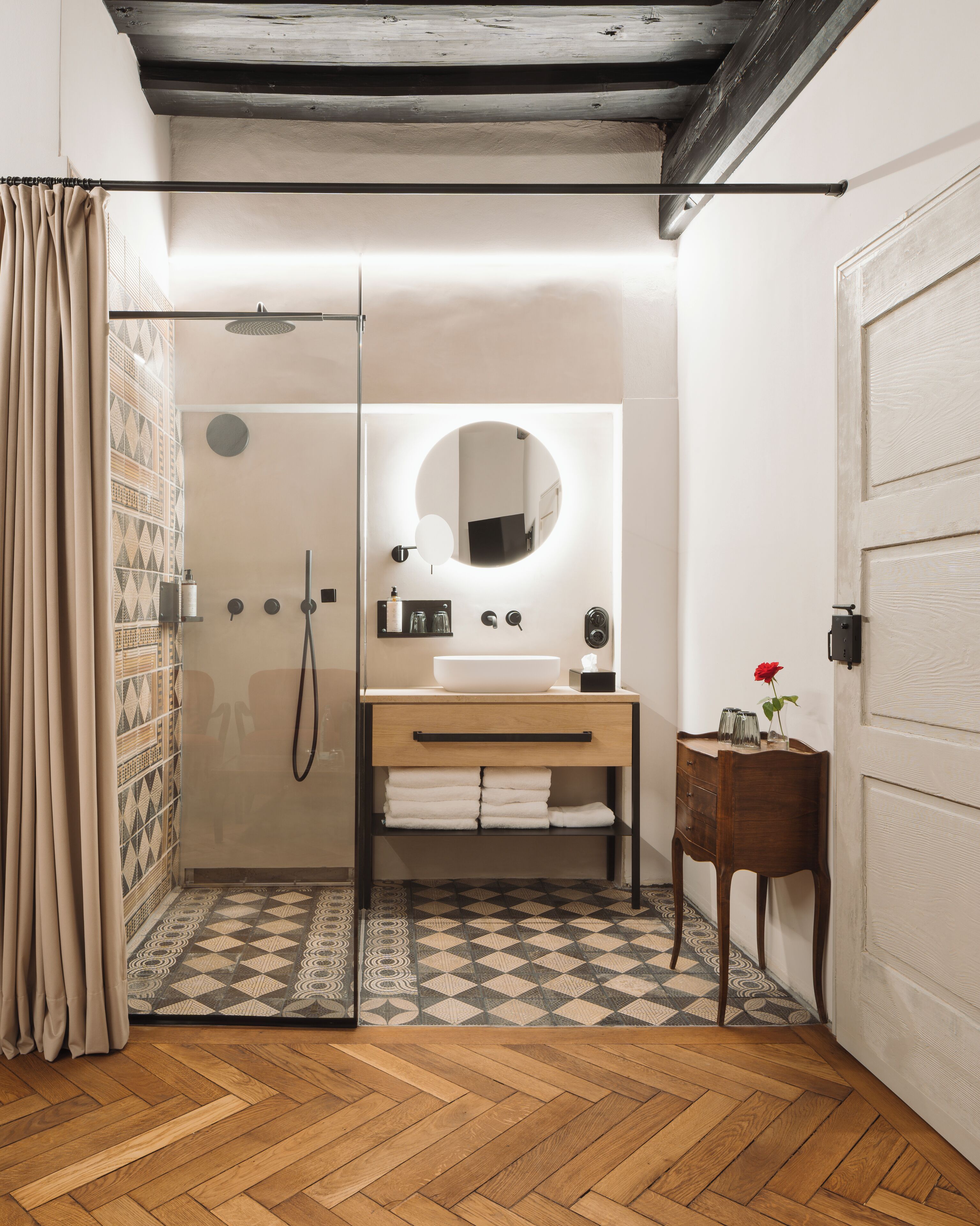 A bathroom with a glass shower enclosure, a wooden vanity with a mirror, and a herringbone-patterned floor.