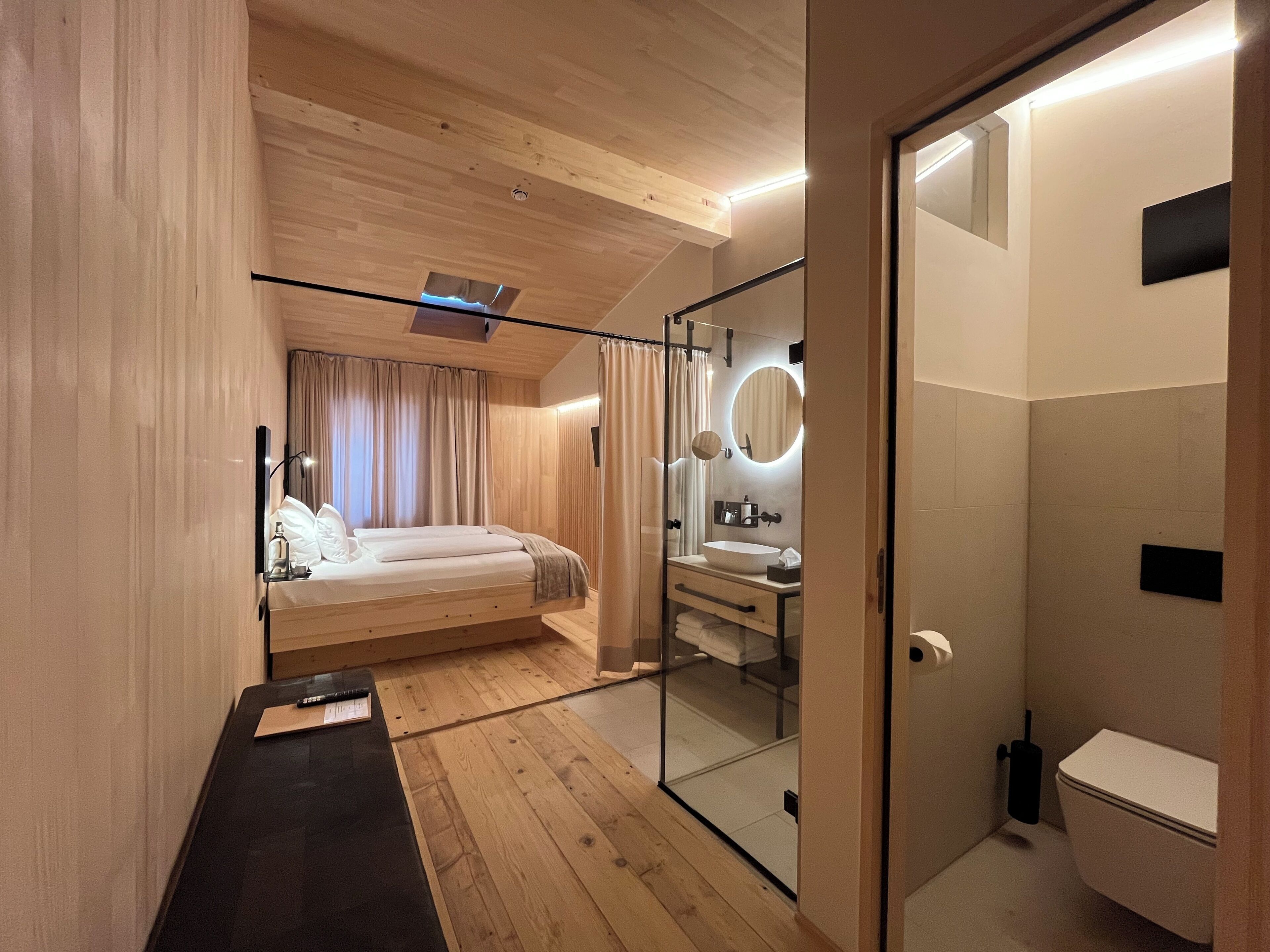A modern bedroom with a wooden ceiling, a glass shower enclosure, a bedside table, and a large bed.