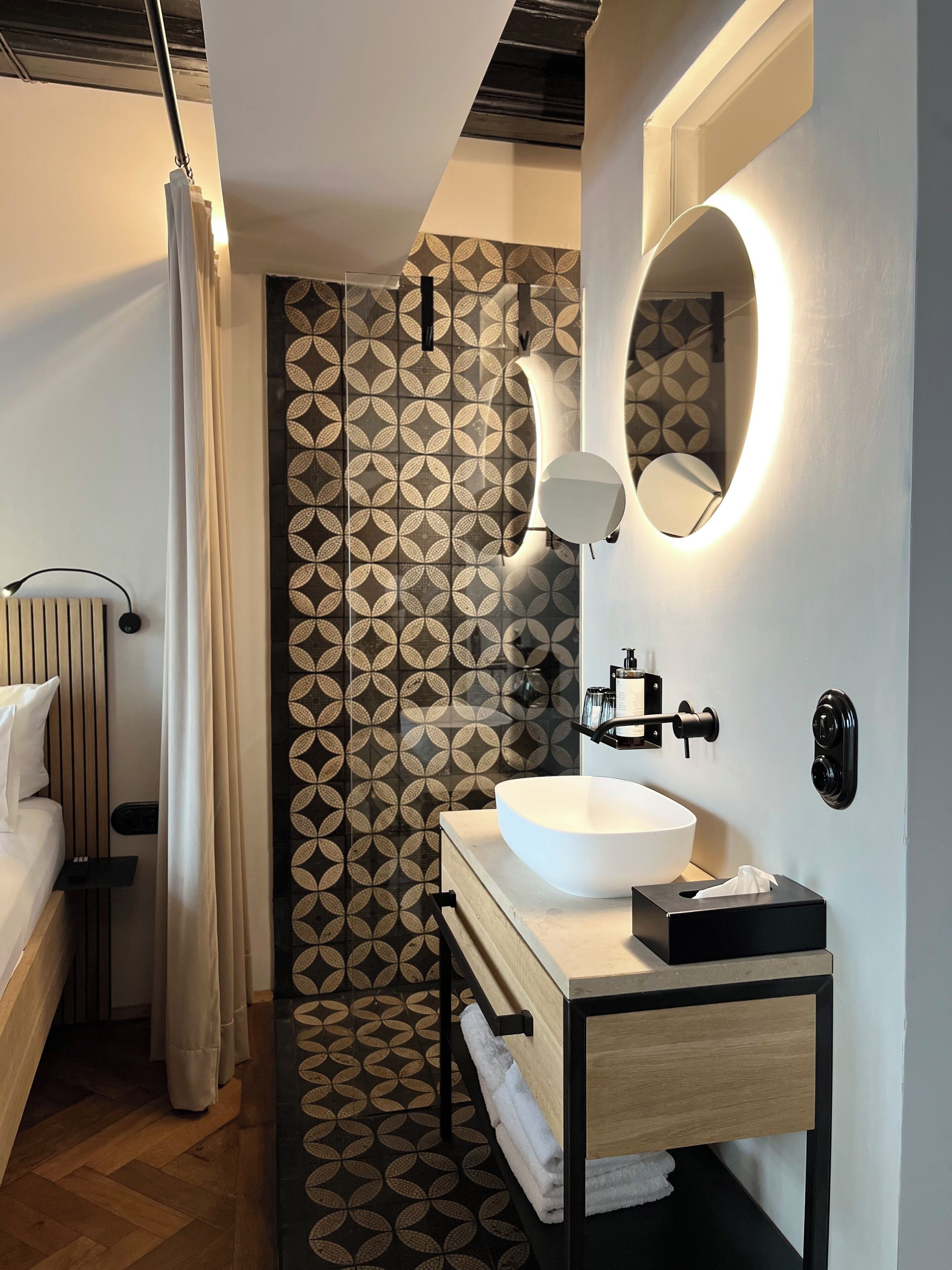 A modern bathroom with a large white sink, a mirror, and a patterned wall.