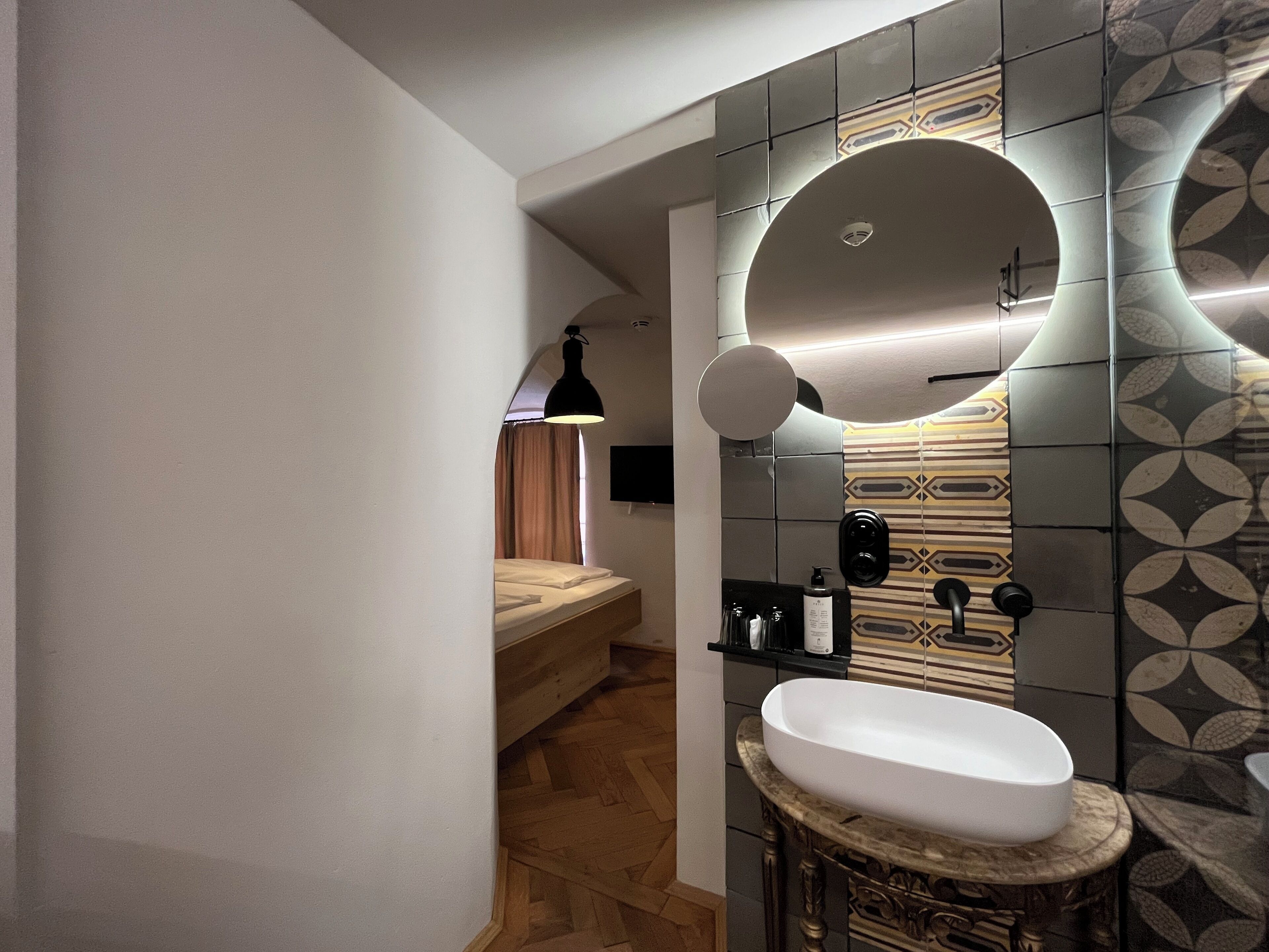 A modern bathroom with a large mirror, a round sink, and a wooden bench.