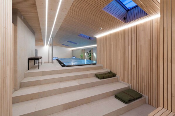 A modern interior with a wooden staircase leading to a spa area, including a hot tub and a seating area with cushions.