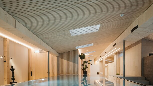 A modern indoor swimming pool with a glass floor, wooden panel walls, and recessed lighting. - Hotel Kühbacher (Passau)