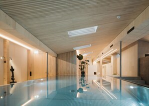 A modern indoor swimming pool with a glass floor, wooden panel walls, and recessed lighting. - Hotel Kühbacher (Passau)
