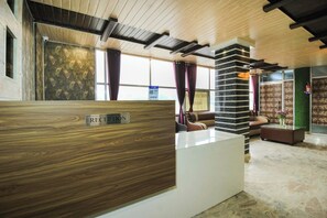 A reception area with a wooden reception desk, a marble floor, and a seating area with a sofa and armchairs. - Hotel Mehraz (Haldwani)