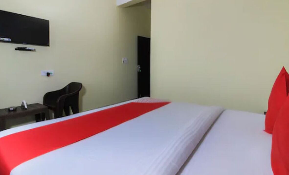 Una habitación de hotel con cama, escritorio, silla y televisor en la pared.