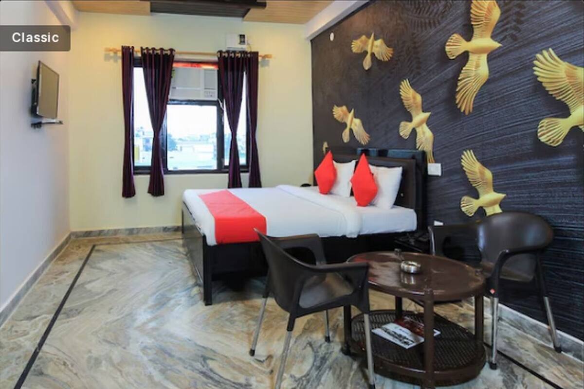 Hotelkamer met een bed, twee stoelen, een klein tafeltje, een raam met gordijnen en een muur met een vogelmuurschildering.