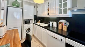 A compact kitchen with white cabinets, a black countertop, a washing machine, a microwave, a Bosch dishwasher, and a green vase on the fridge. - Savannah apartment near Carlton (Cannes)