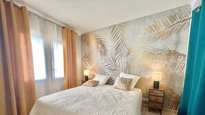 A hotel room with a large bed, two bedside tables with lamps, a tropical leaf-patterned wall, and a view of the outdoors through the window. - Savannah apartment near Carlton (Cannes)