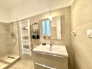 Un baño moderno con cabina de ducha de vidrio, un toallero blanco, un lavabo con espejo y una ventana pequeña que proporciona luz natural.