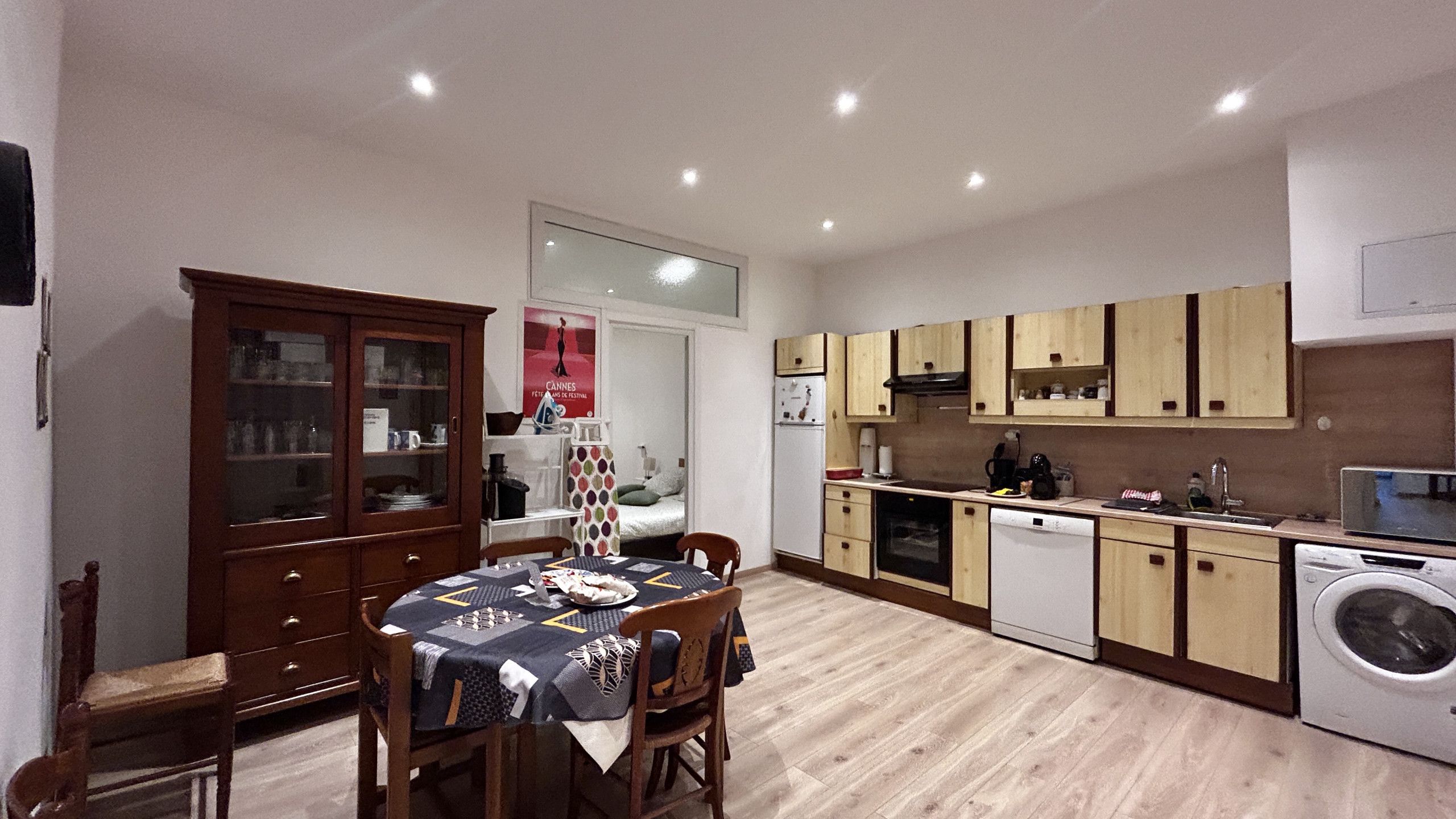 A compact kitchen with wooden cabinets, a dining table with chairs, and a washing machine.