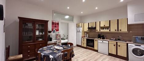 A compact kitchen with wooden cabinets, a dining table with chairs, and a washing machine.