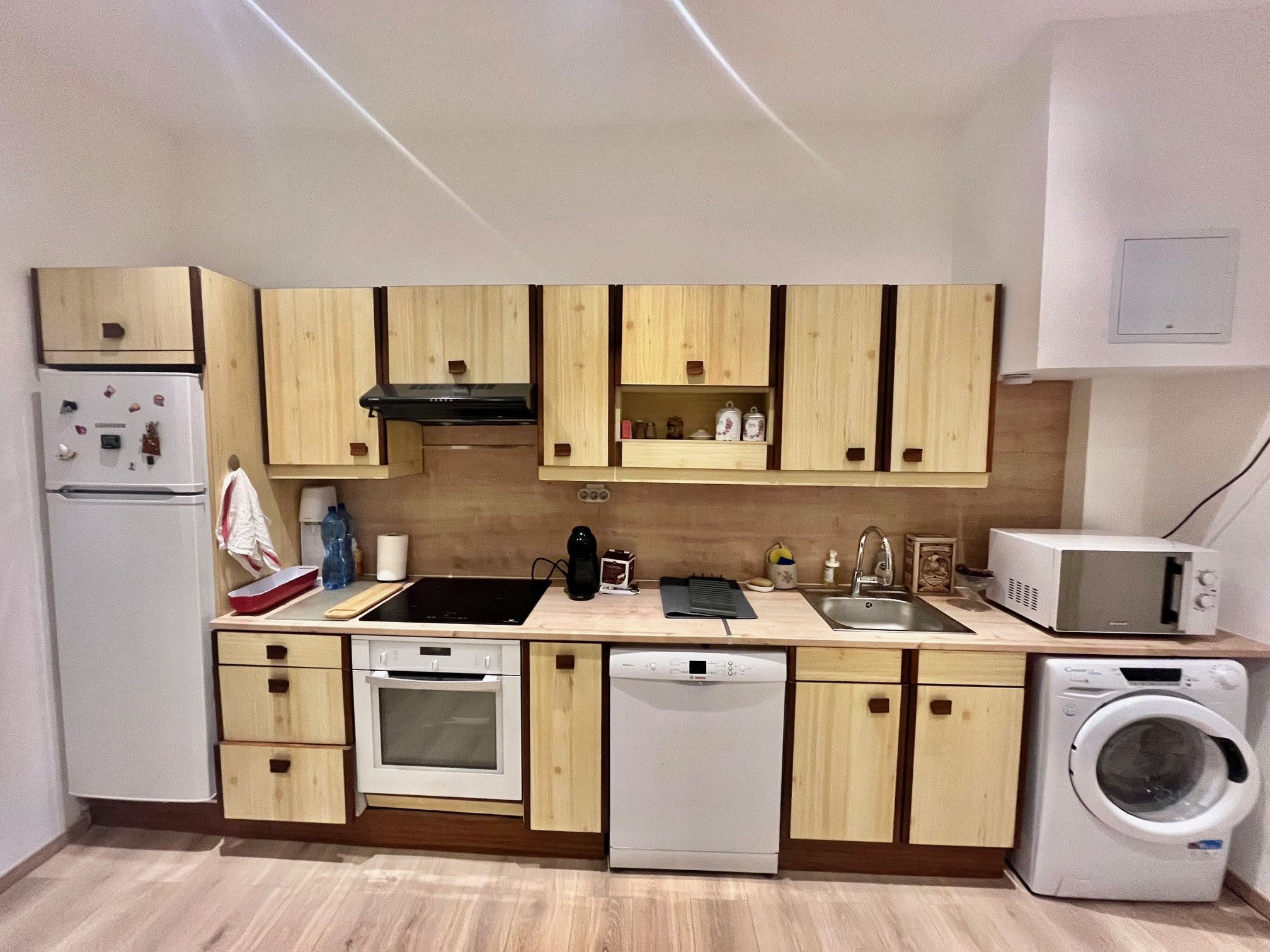 A compact kitchen with wooden cabinets, a built-in oven, a dishwasher, a microwave, and a washing machine.