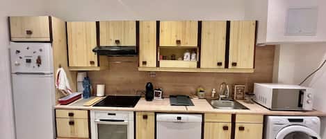 A compact kitchen with wooden cabinets, a built-in oven, a dishwasher, a microwave, and a washing machine.