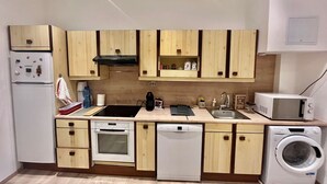 A compact kitchen with wooden cabinets, a built-in oven, a dishwasher, a microwave, and a washing machine. - woody (Cannes)