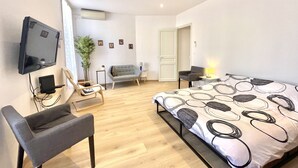 A modern hotel room with a bed, a desk, a chair, a TV, and a plant. - woody (Cannes)